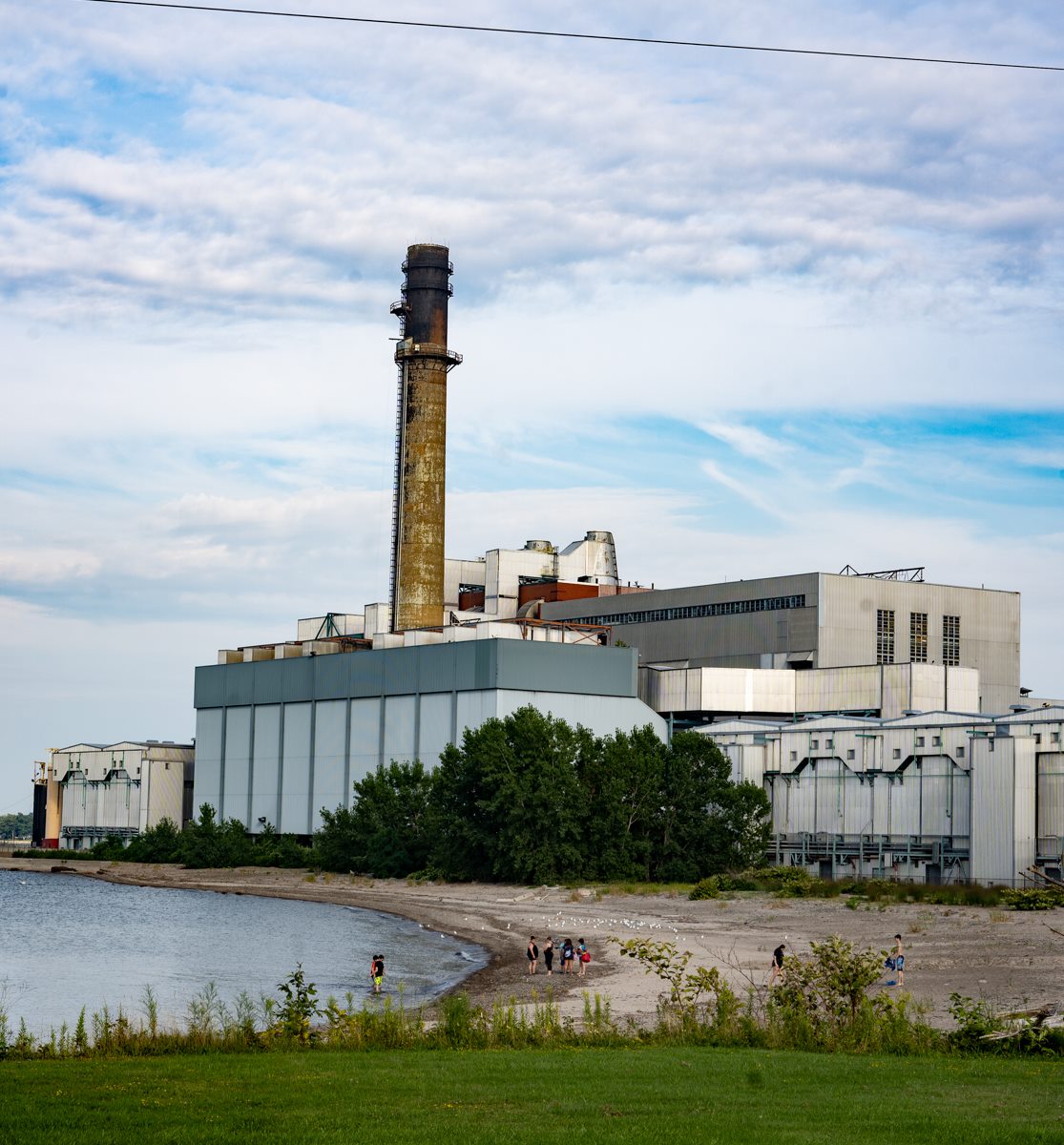 people swimming on beach next to power station